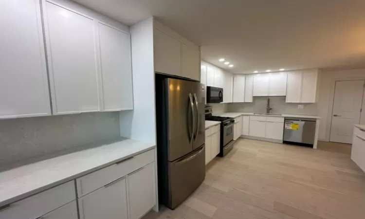 Kitchen with decorative backsplash, appliances with stainless steel finishes, light hardwood / wood-style floors, and white cabinetry