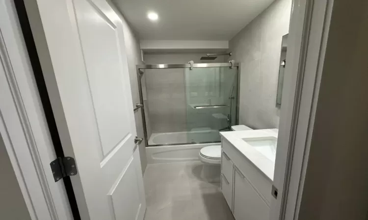 Full bathroom featuring shower / bath combination with glass door, vanity, and toilet