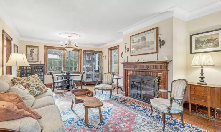 Living room with wood-type flooring, an inviting chandelier, a brick fireplace, and ornamental molding