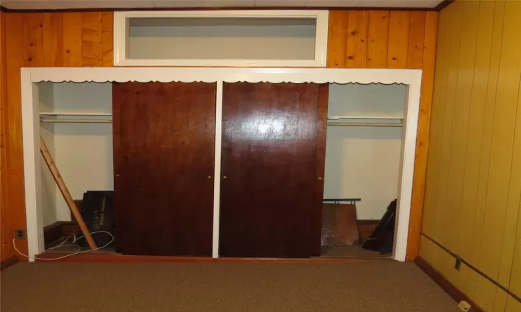 Unfurnished bedroom featuring wood walls and carpet