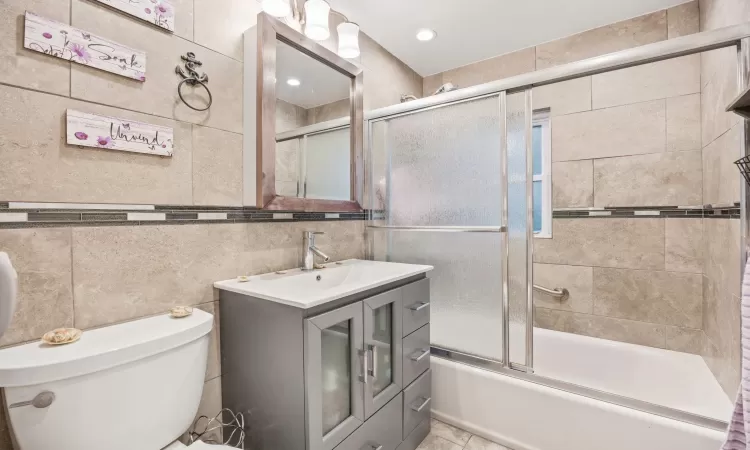 Full bathroom with shower / bath combination with glass door, vanity, tile walls, and toilet