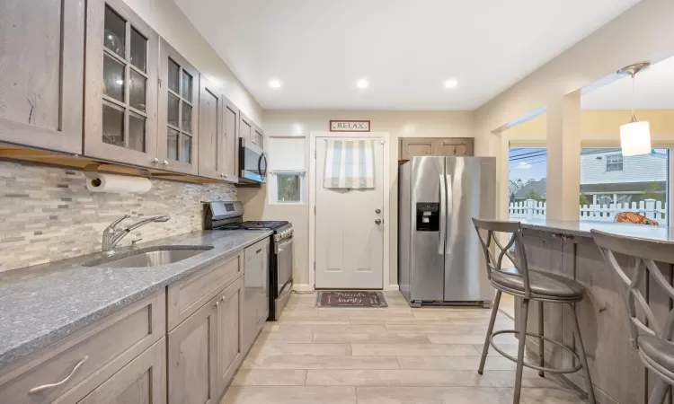 Kitchen with appliances with stainless steel finishes, light wood-type flooring, light stone counters, sink, and hanging light fixtures