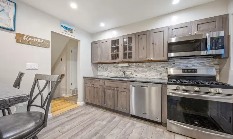 Kitchen featuring sink, backsplash, dark stone countertops, light hardwood / wood-style floors, and appliances with stainless steel finishes