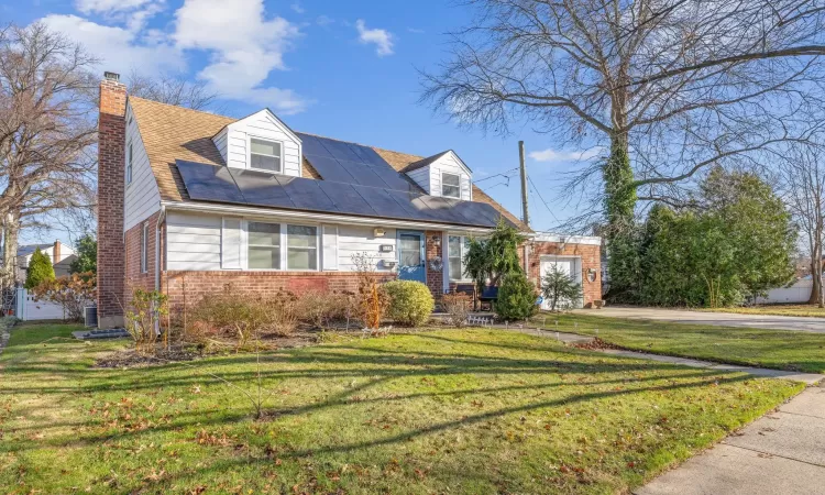 Cape cod-style house featuring solar panels, a garage, and a front lawn