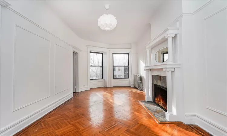 Unfurnished living room featuring a tiled fireplace, radiator heating unit, and parquet floors