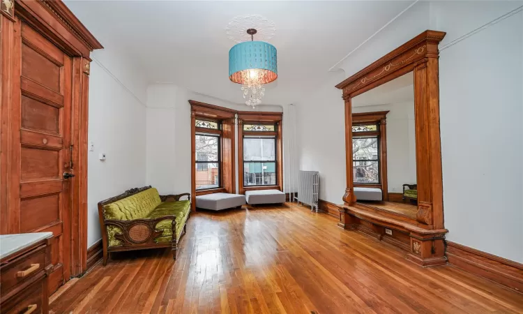 Unfurnished room featuring radiator, wood-type flooring, a wealth of natural light, and an inviting chandelier