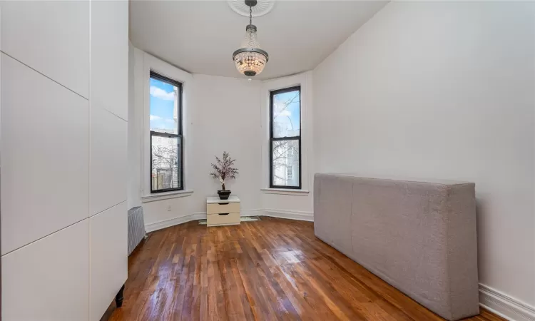 Spare room featuring a healthy amount of sunlight, dark wood-type flooring, radiator, and a chandelier