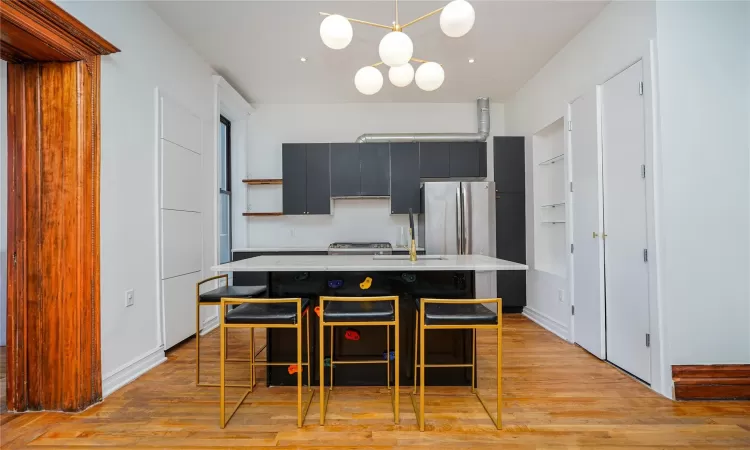 Kitchen with a kitchen breakfast bar, stainless steel appliances, a kitchen island with sink, pendant lighting, and light hardwood / wood-style flooring