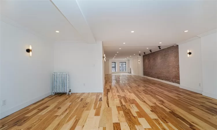 Empty room featuring light wood-type flooring, radiator, ornamental molding, and brick wall