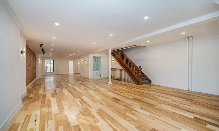 Unfurnished living room featuring crown molding, brick wall, and light hardwood / wood-style flooring