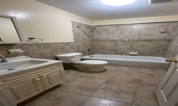 Full bathroom featuring vanity, tiled shower / bath combo, toilet, and tile walls