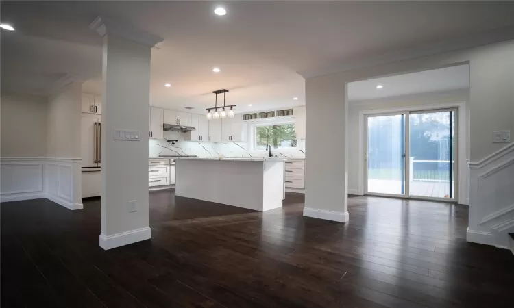 Kitchen with a center island, white cabinets, dark wood-type flooring, and decorative light fixtures