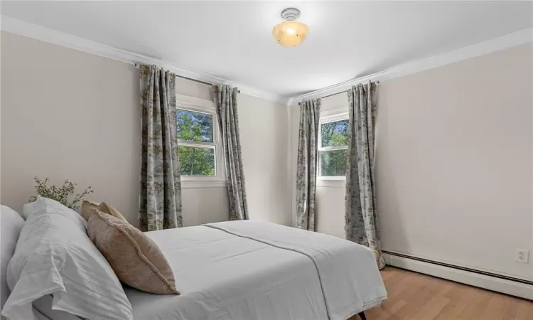 Bedroom featuring a baseboard heating unit, crown molding, and hardwood / wood-style flooring