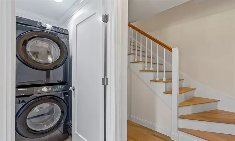 Laundry area featuring ornamental molding, stacked washer and dryer, and light wood-type flooring