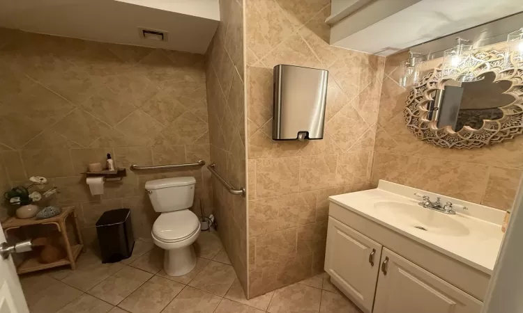 Bathroom featuring tile patterned flooring, vanity, tile walls, and toilet