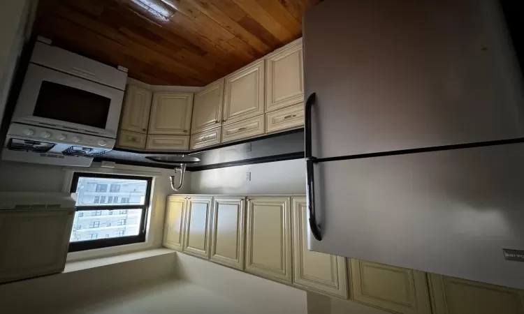 Kitchen with cream cabinetry, refrigerator, stove, and sink