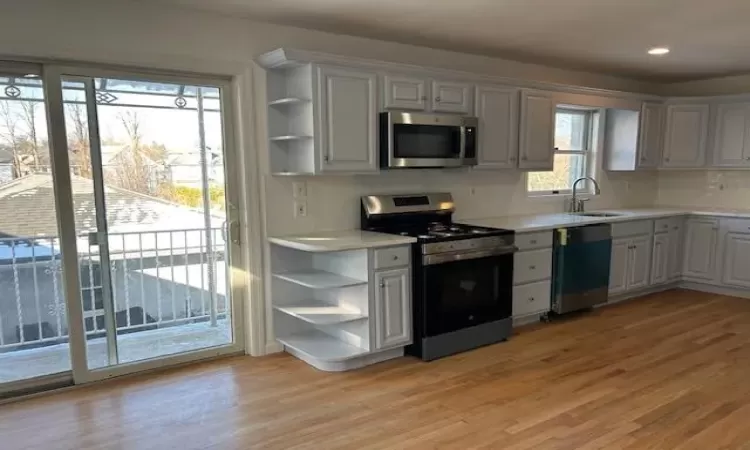 Kitchen featuring sink, tasteful backsplash, light hardwood / wood-style floors, white cabinetry, and stainless steel appliances