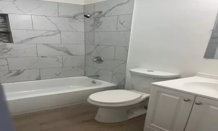 Full bathroom with hardwood / wood-style floors, vanity, tiled shower / bath combo, and toilet