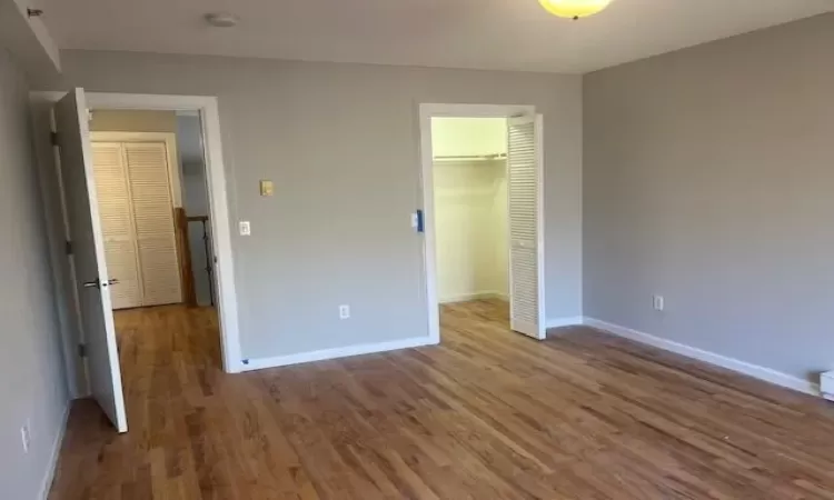 Unfurnished bedroom featuring a walk in closet, a closet, and wood-type flooring