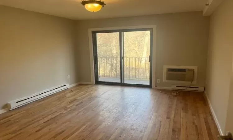 Spare bedroom with hardwood flooring, an AC wall unit, and a baseboard radiator