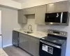 Kitchen with appliances with stainless steel finishes, light stone counters, sink, wood-type flooring, and gray cabinets