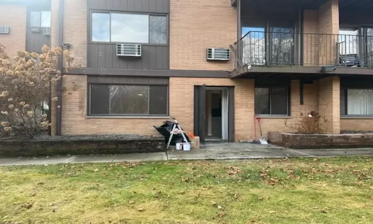 Back of property featuring a yard, a balcony, a wall unit AC, and a patio