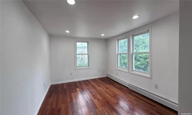 Empty room with dark wood-type flooring and a baseboard heating unit