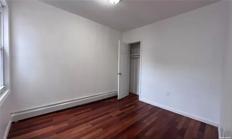 Unfurnished bedroom with dark hardwood / wood-style floors, a closet, and a baseboard heating unit