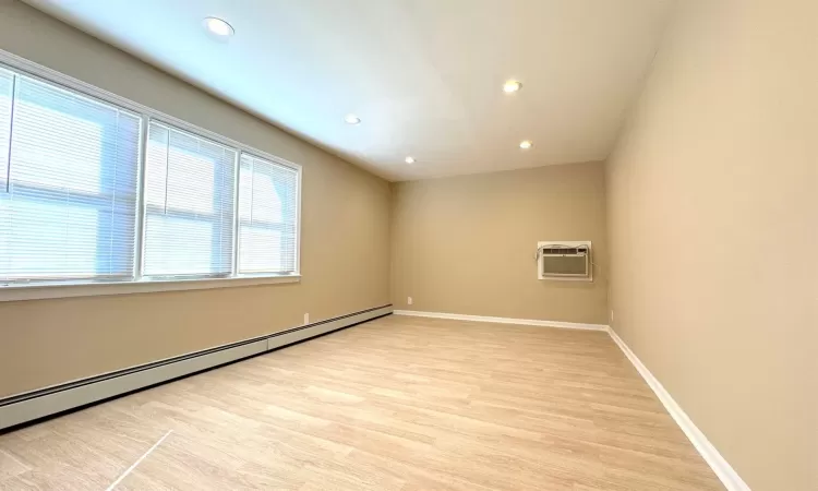 Unfurnished room with light hardwood / wood-style floors, a wall mounted air conditioner, and a baseboard heating unit