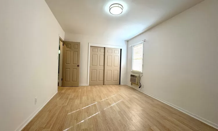 Unfurnished bedroom with a wall mounted AC, a closet, and light hardwood / wood-style flooring