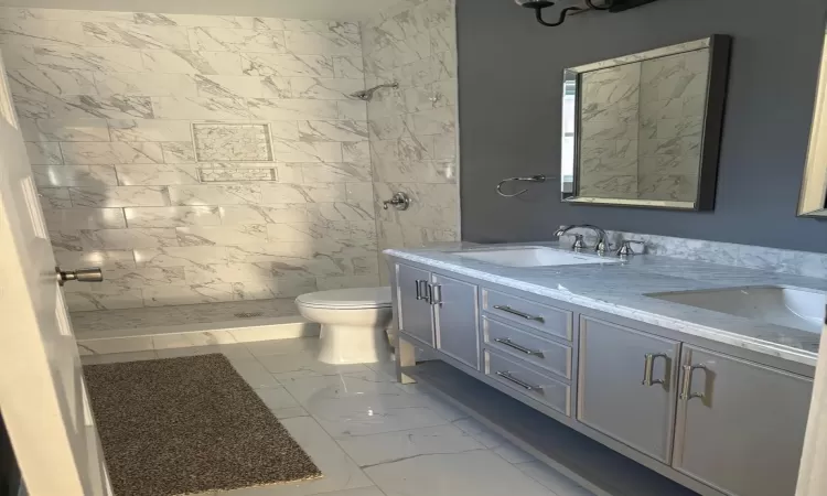 Bathroom featuring toilet, vanity, and tiled shower