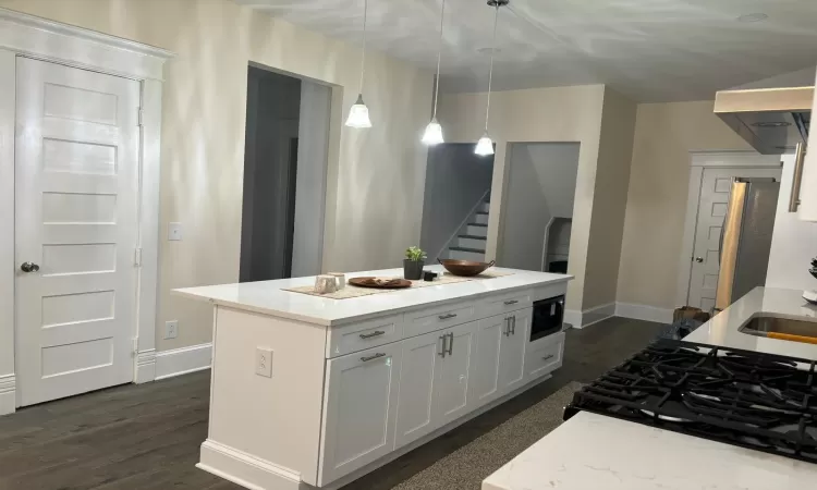 Kitchen with black microwave, a kitchen island, stainless steel fridge, pendant lighting, and white cabinets