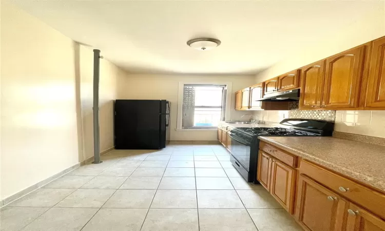 Kitchen with backsplash, sink, light tile patterned floors, and black appliances