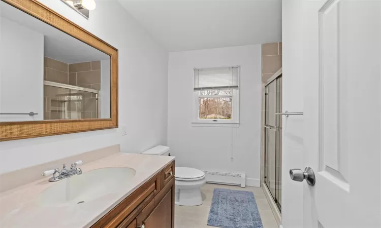 Bathroom with baseboard heating, tile patterned flooring, toilet, a shower with door, and vanity