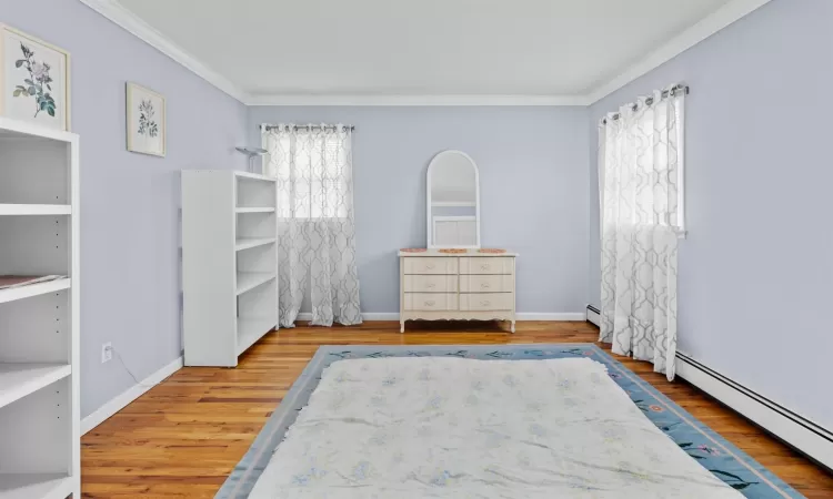 Unfurnished bedroom with multiple windows, crown molding, a baseboard radiator, and hardwood / wood-style flooring