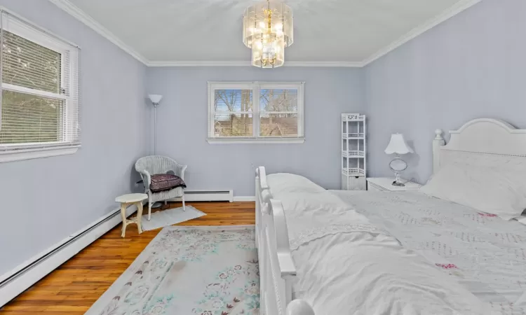 Bedroom featuring hardwood / wood-style flooring, an inviting chandelier, ornamental molding, and a baseboard heating unit