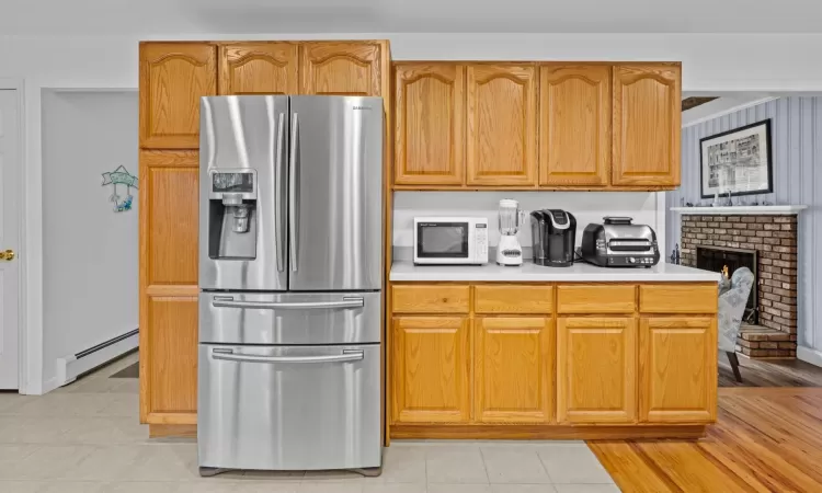 Kitchen featuring a brick fireplace, stainless steel fridge with ice dispenser, and a baseboard heating unit