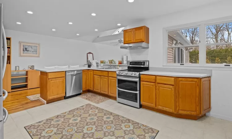 Kitchen featuring ventilation hood, sink, light tile patterned floors, appliances with stainless steel finishes, and kitchen peninsula