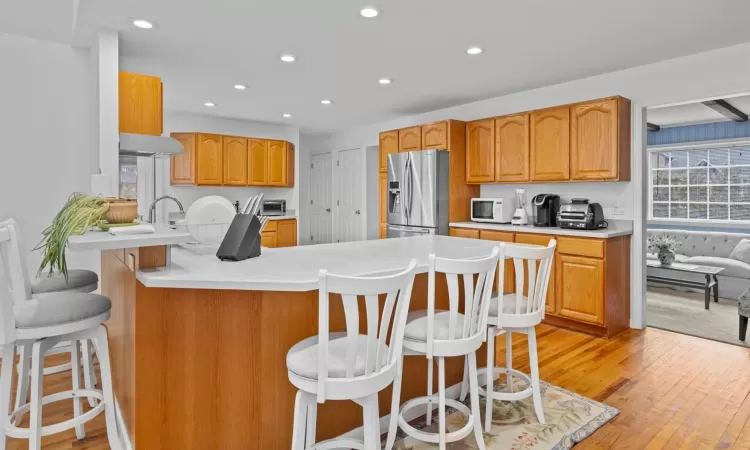 Kitchen featuring a kitchen breakfast bar, kitchen peninsula, range hood, light hardwood / wood-style floors, and stainless steel fridge with ice dispenser