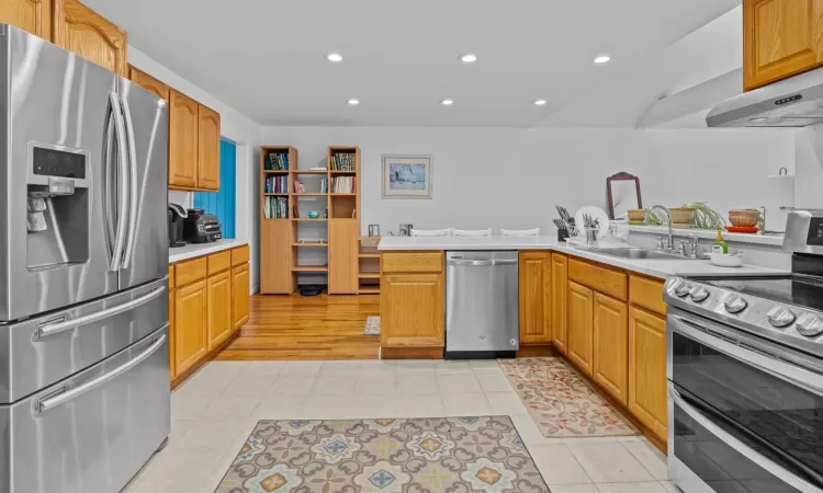 Kitchen with exhaust hood, sink, light tile patterned floors, kitchen peninsula, and stainless steel appliances