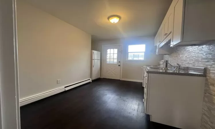 Kitchen with dark wood-type flooring, white cabinets, tasteful backsplash, white fridge, and a baseboard radiator