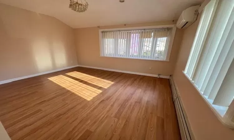 Spare room featuring hardwood / wood-style flooring, a baseboard radiator, a wall unit AC, and vaulted ceiling