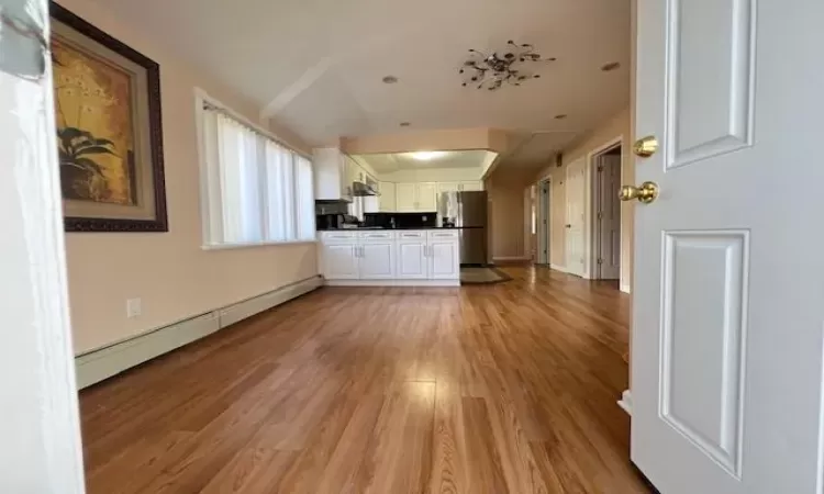 Unfurnished living room featuring light hardwood / wood-style floors, vaulted ceiling, and a baseboard heating unit