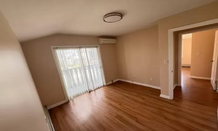 Empty room featuring vaulted ceiling, dark hardwood / wood-style floors, and a wall mounted air conditioner