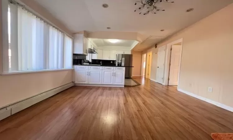 Kitchen with stainless steel refrigerator, white cabinetry, a baseboard radiator, light hardwood / wood-style flooring, and vaulted ceiling