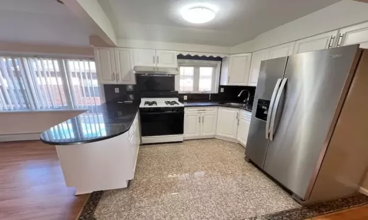 Kitchen featuring sink, stainless steel fridge with ice dispenser, white range oven, kitchen peninsula, and white cabinets