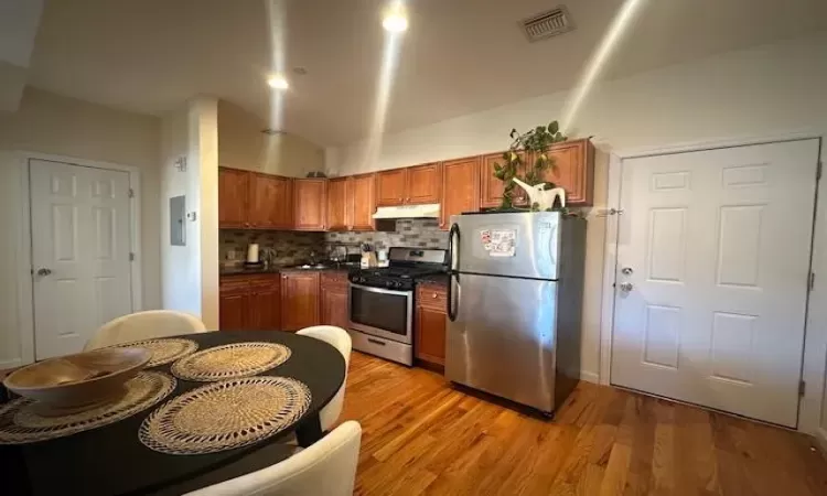 Kitchen featuring decorative backsplash, electric panel, wood-type flooring, and appliances with stainless steel finishes