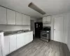 Kitchen with sink, stainless steel gas range oven, black fridge, light hardwood / wood-style flooring, and white cabinets