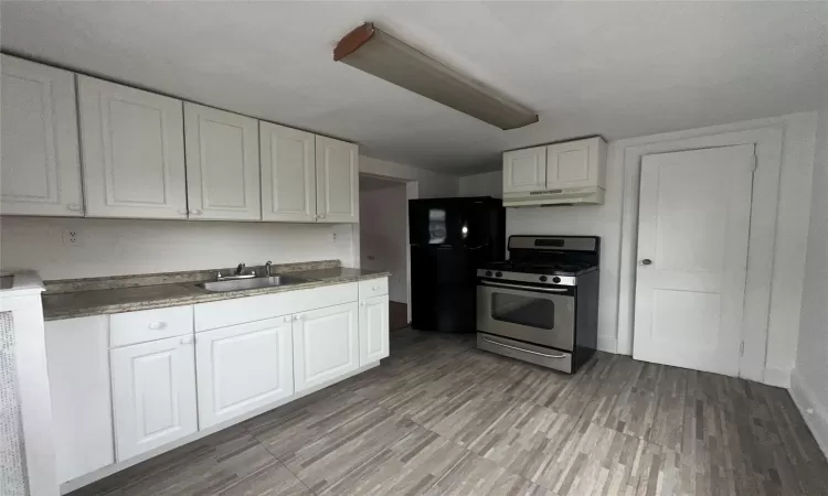 Kitchen with sink, stainless steel gas range oven, black fridge, light hardwood / wood-style flooring, and white cabinets