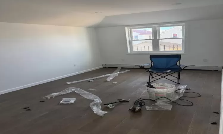 Unfurnished room featuring dark hardwood / wood-style flooring, a baseboard radiator, and vaulted ceiling